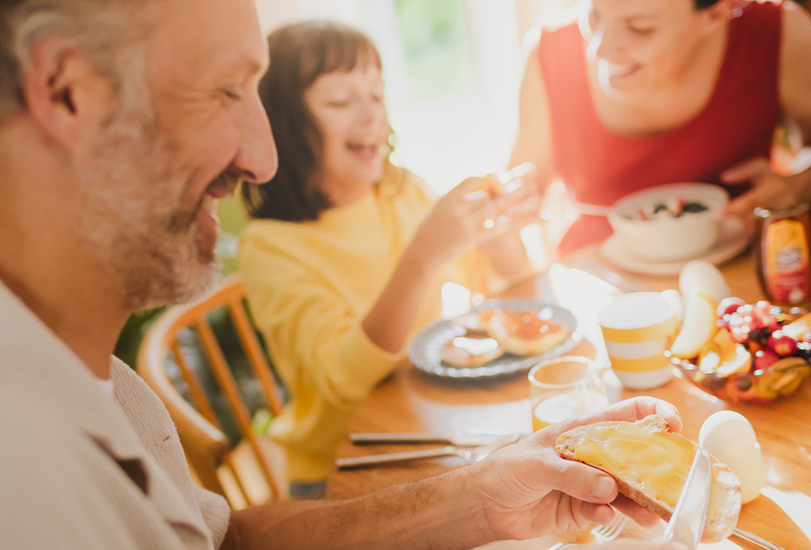 Familie sitzt am Tisch. Der Vater schiert sich ein Brot mit leckerem Langnese Honig.